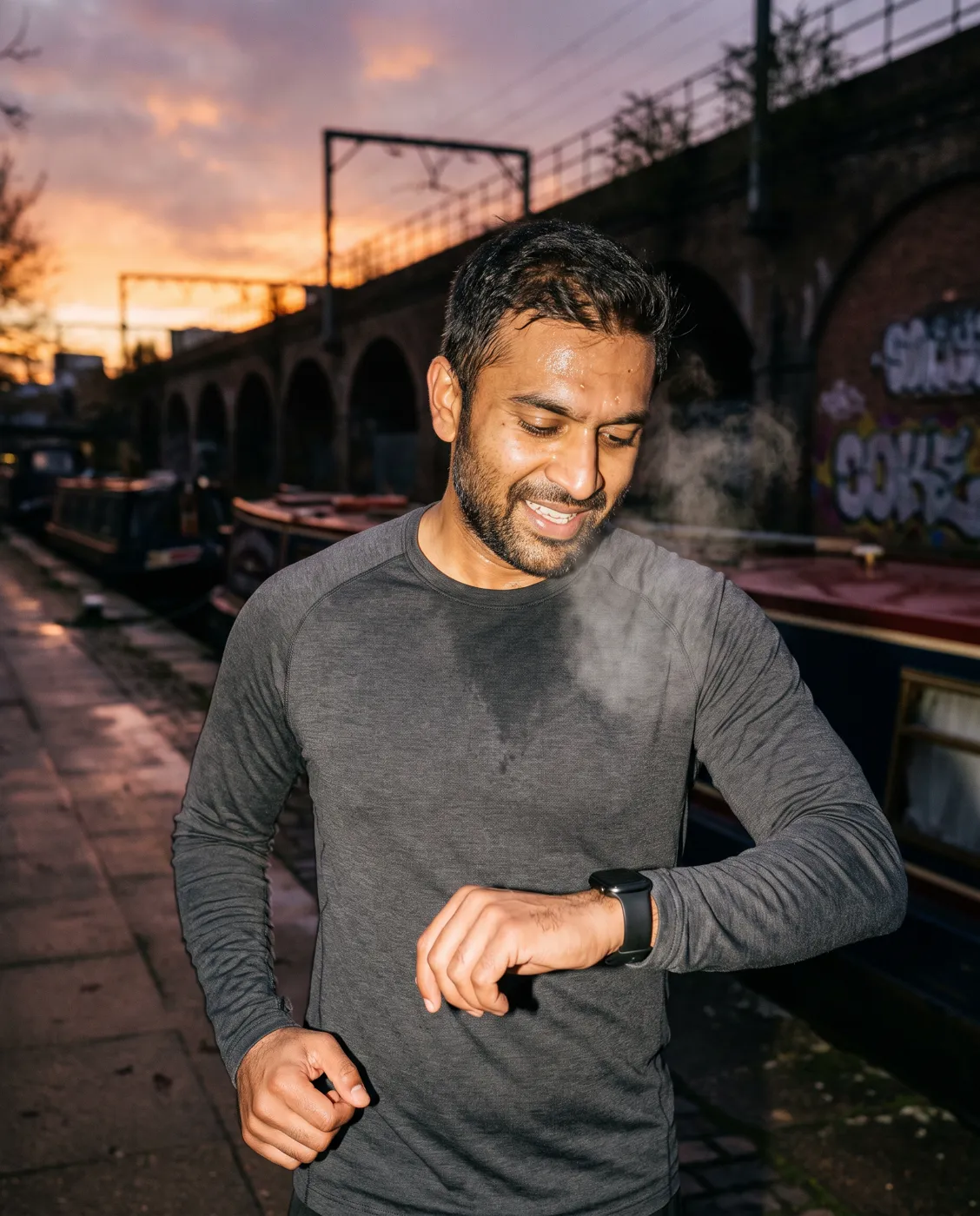 Runner checking his smartwatch on an East London canal towpath at dawn